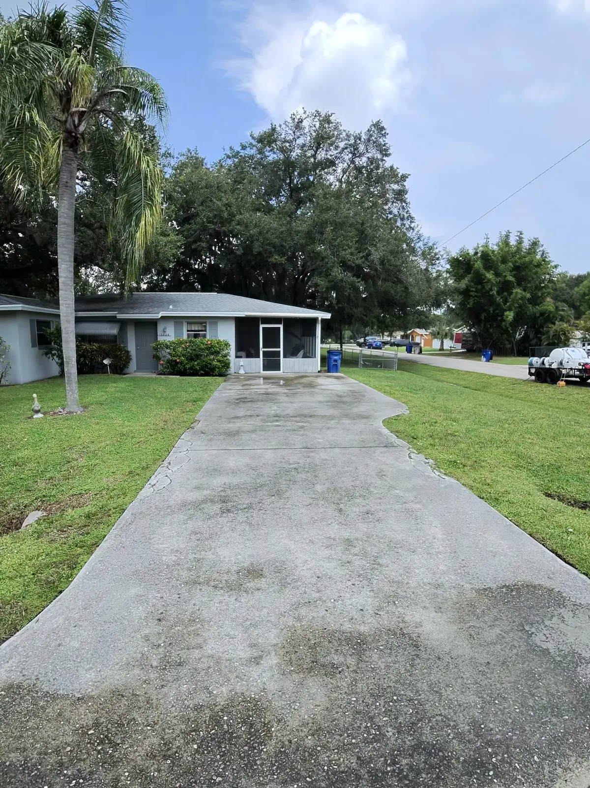 A long concrete driveway leading to a house with a screen enclosure and a palm tree.