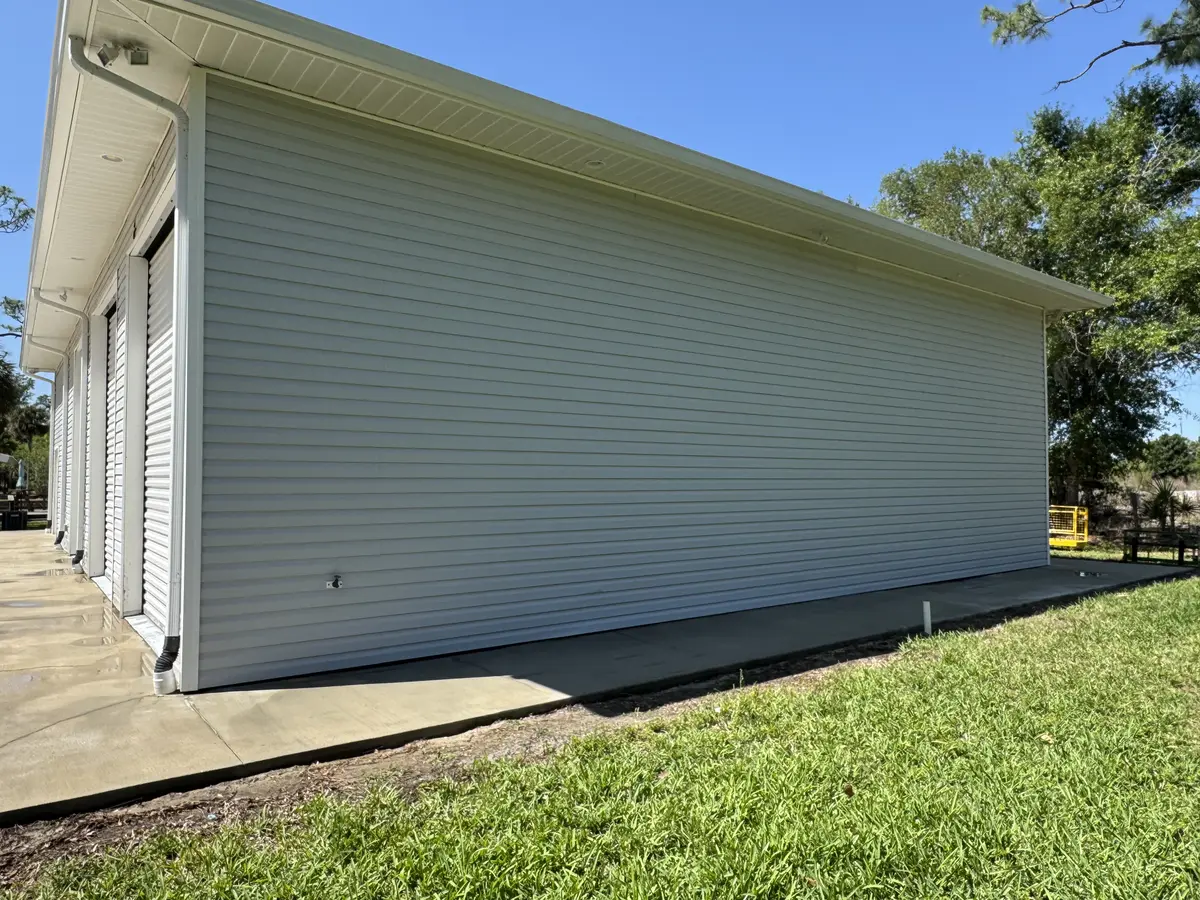 A cleaned wall of light-coloured siding beside a concrete path and lawn.