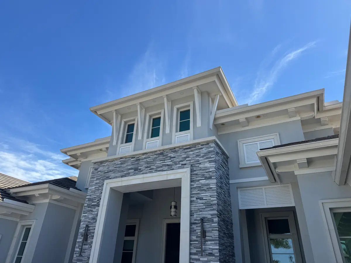 The front of a multi-story home with grey walls and stone accents under a blue sky.