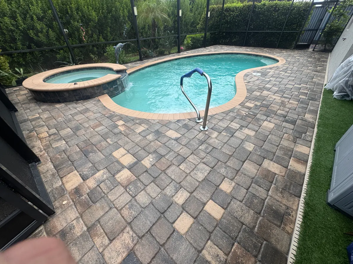 A backyard pool and stone paver deck inside a screened enclosure.
